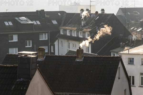 Smoke plume from a chimney over densely built residential area in the evening light, wintry city