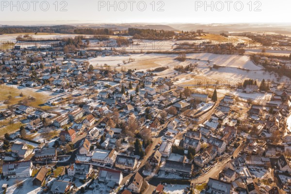 Aerial view of a snowy village with adjacent fields in the soft light of a winter sunset,