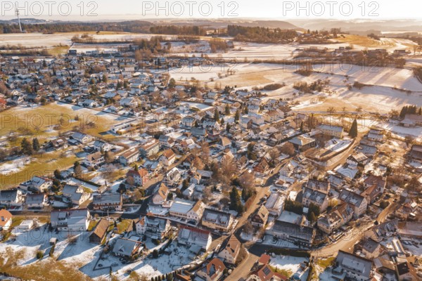 Wide settlement in winter with snow-covered roofs and fields in sunlight from an aerial