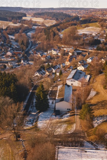 Small settlement with snow-covered houses and roads, surrounded by forest landscape, Aach,