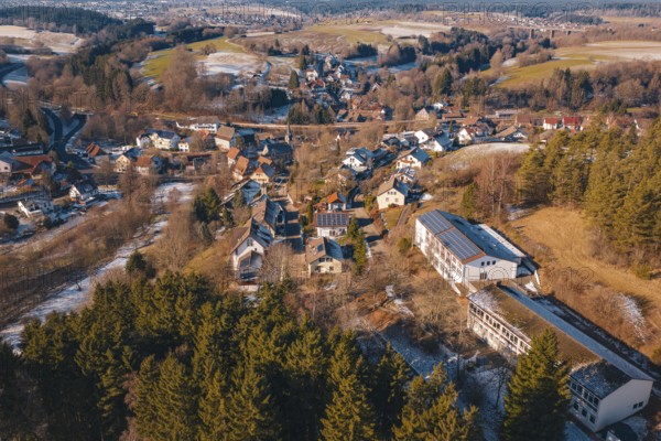 Panoramic view of a village with snow-covered roofs surrounded by forest and hills, Aach,