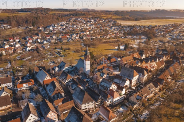 Aerial view of a town with church and buildings in evening light, surrounded by hills and fields,