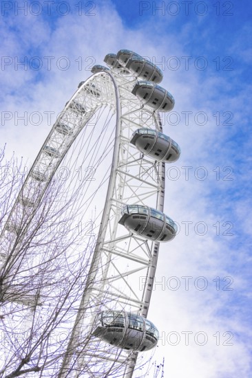 A large Ferris wheel juts into the blue sky surrounded by clouds, London Eye, London, United