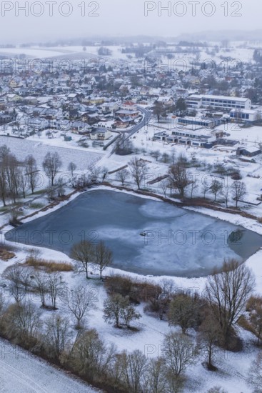 Snowy village with frozen lake seen from above on a grey day, Empfingen, Freudenstadt district,