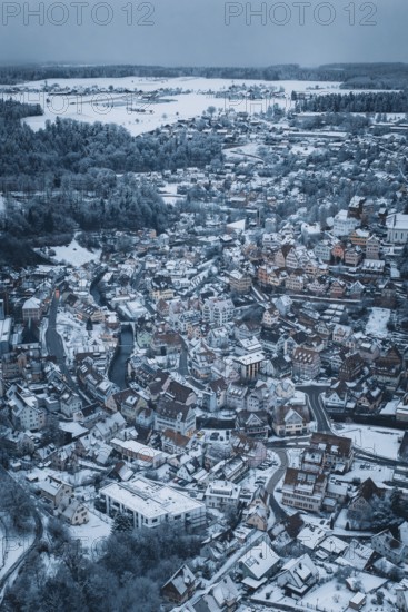 A snow-covered city from the air with many houses and a river, surrounded by hills and forests in a