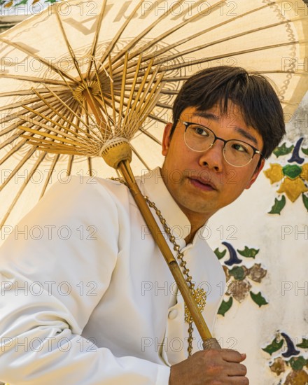 Young man wearing a parasol in traditional clothing presents himself for the photographers, Wat