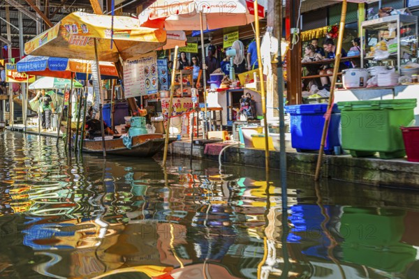 Wooden boat and umbrellas are reflected on the Damneon Saduak floating market channel near Bangkok,