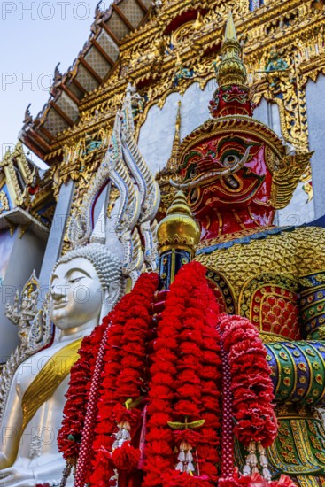 Richly decorated Buddha statue at Wat Suthiwararam Buddhist temple, guarded by a yaksha, Bangkok,