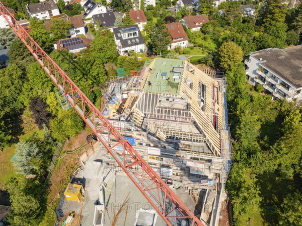 Crane over a construction site with an unfinished roof and surrounding residential buildings,