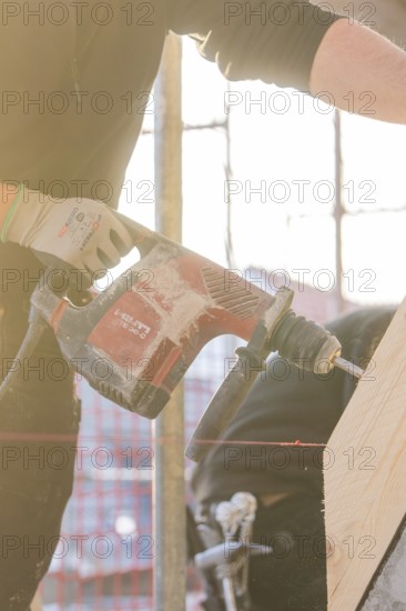 Close-up of workers with drill, wood and sunlight on construction site, carpentry construction,