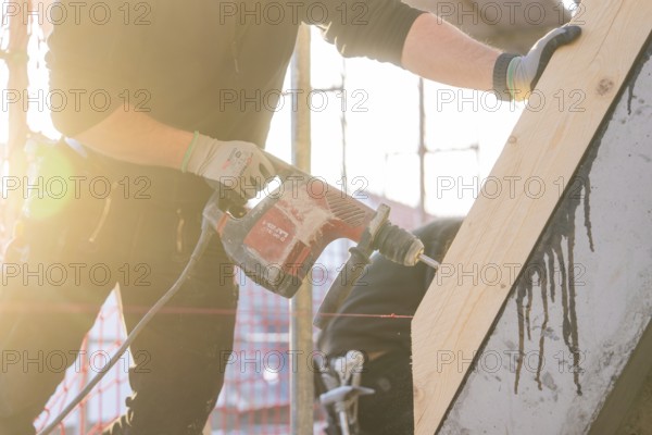Worker with drill in sunlight working on wood on construction site, carpentry construction, roof
