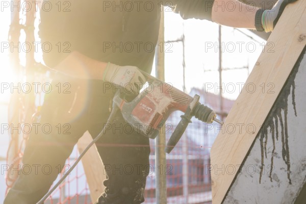 Construction worker drilling wood elements on construction site in sunlight, carpentry construction