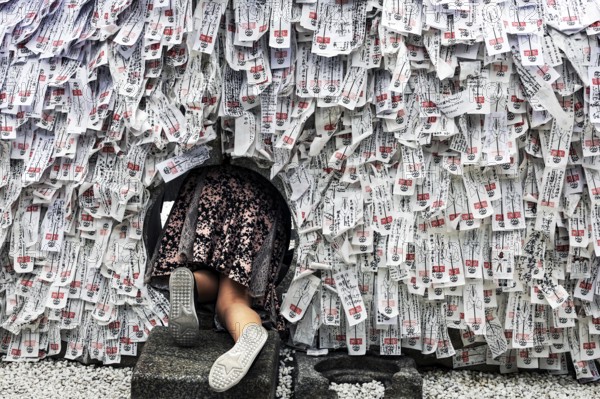 Person crawling through hole in stone with strips of paper in Yasui Konpiragu Temple, Kyoto, Gion,