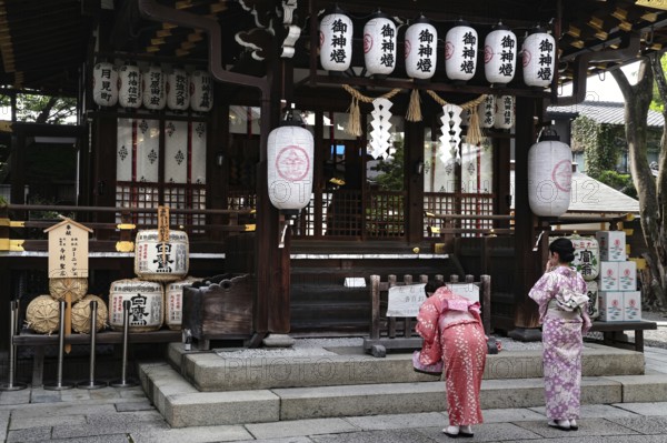 Two woman wearing kimono praying to traditional lanterns at Yasui Konpiragu Temple, Kyoto, Gion,