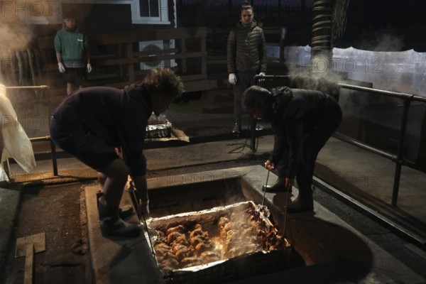 Preparing a traditional hangi in a pit with steam and people in Rotorua, Rotorua, Bay of Plenty,