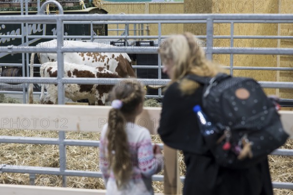 A mother and her daughter in front of a cowshed in the animal shed at the Green Week at the