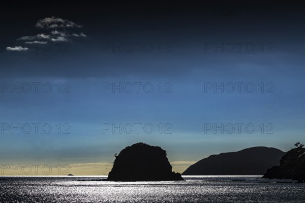 A silhouette of an island against a dark blue sky at sunset, Bay of Islands, New Zealand