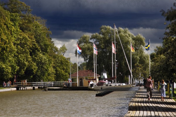 Söderköping harbour on Göta Canal with flags and trees under a cloudy sky, Söderköping, Sweden