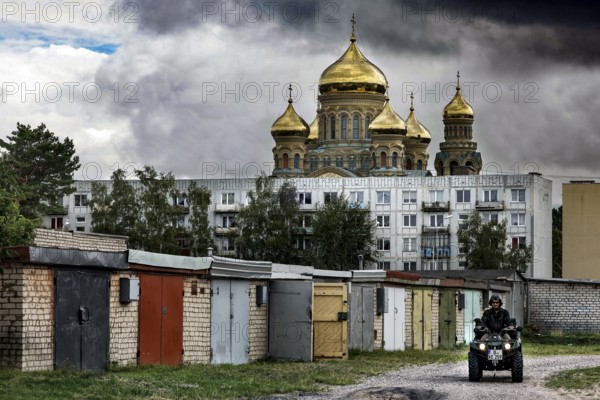 In front of an imposing church, golden domes rise above prefabricated buildings and garages,