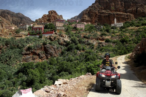 Quad driver on a trail through a mountainous village and green surroundings, Anergui, zero, Morocco
