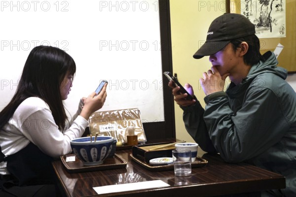 A couple is sitting in a restaurant in Kurashiki, both engrossed in their smartphones, Kurashiki,