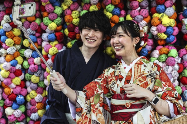Couple wearing kimonos taking selfies in front of colorful backgrounds at Yasaka Koshindo Temple,