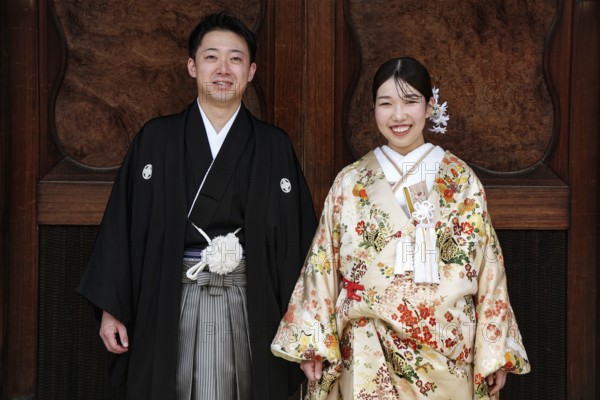 Bride and groom wearing traditional kimonos against a wooden background, Kyoto, Higashiyama, Japan