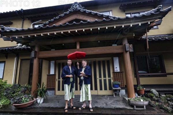 Two people with red umbrellas in front of a traditional ryokan in Aso, Aso, Kumamoto, Japan