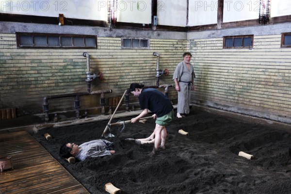 A sand bath at Takegawara Onsen Beppu, one person being cared for by another, Beppu, Oita, Japan