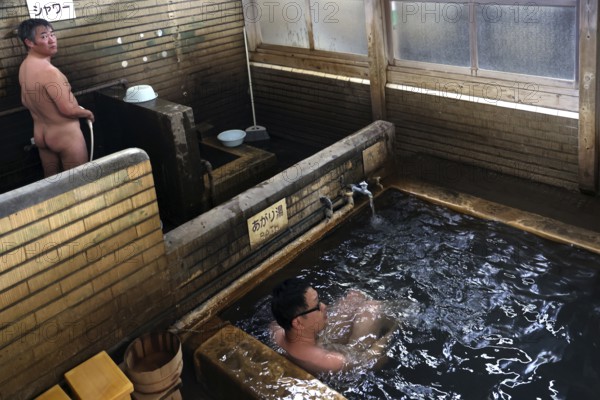 Traditional Japanese onsen bath with wooden walls in a warm setting. People enjoy the relaxing