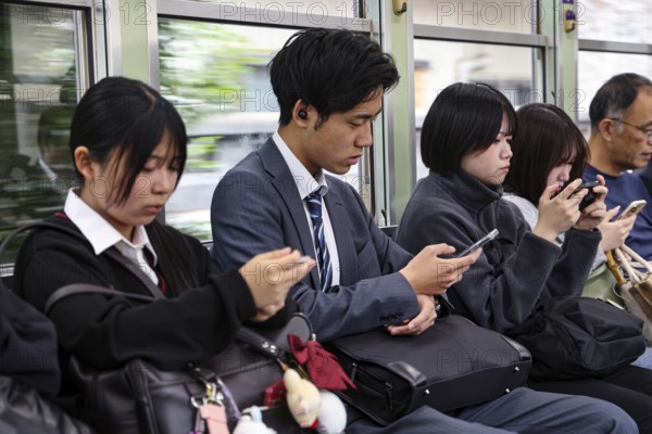 Passengers on a train in Kyoto, including a salaryman, use their smartphones, Arashiyama, Kyoto,