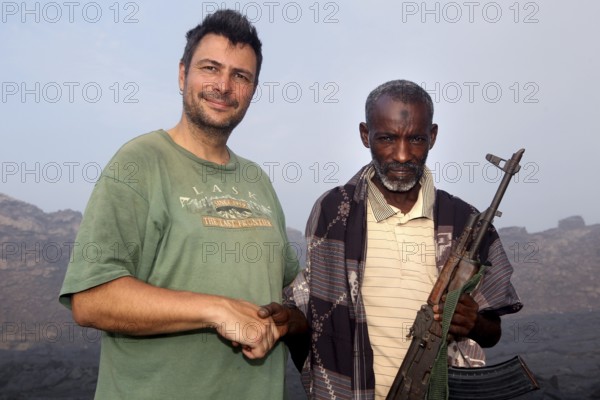 Police officer Muhammed stands next to a man in the volcanic landscape of Erta Ale, Erta Ale, Afar,