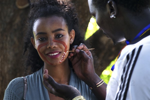 Tourist receives face painting from a hammer during an initiation ritual, outdoor cultural