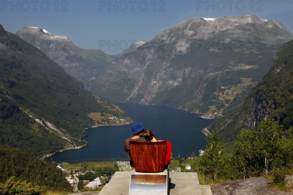 Tourist sits on a red chair and looks at the impressive panorama of Geirangerfjord, Flydalsjuvet,