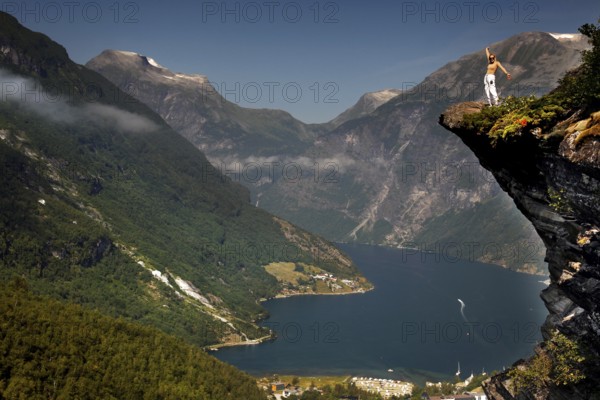 Adventurous tourist stands on cliff and enjoys views of Geirangerfjord, Flydalsjuvet,
