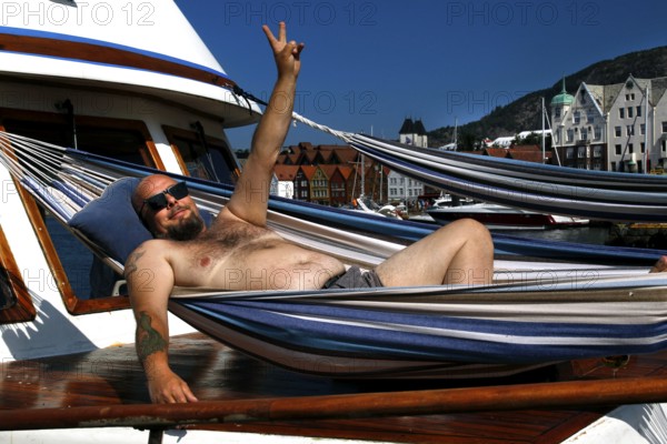 A man poses relaxed in his hammock on a boat in the harbor off Tyskebryggen, Bergen, Norway