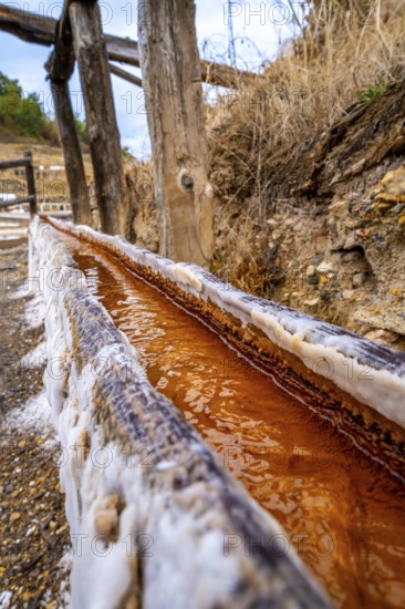 Close up view of the reddish brine flowing along a wooden channel encrusted with salt deposits at