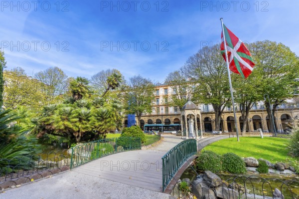 Gipuzkoa plaza park showing lush greenery, a pond with a small bridge, historic buildings, and the