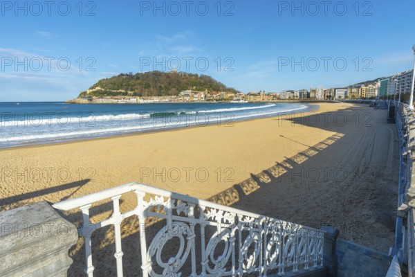 La concha beach view with its iconic promenade railing, golden sand and the city of san sebastian