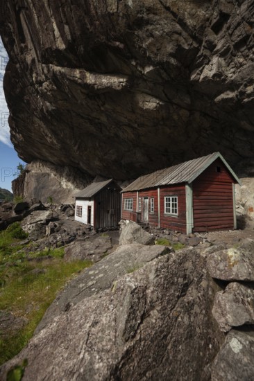 Historical wooden houses sheltered under a massive rock overhang. Summer, Helleren (Helleren),