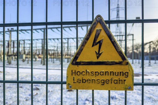 Recording of snow in winter warning sign warning high voltage danger to life on fence from behind