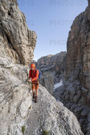 Mountaineer climbs an exposed rock band in the secured via ferrata Bocciere Centrale, Brenta
