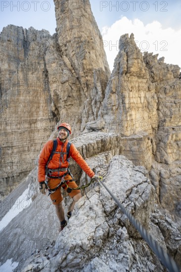 Mountaineer climbs on an exposed rock in the secured via ferrata Bocciere Centrale, Brenta