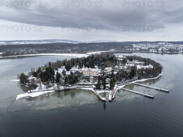 The wintry and snowy Mainau island in Lake Constance with the pier and the baroque Mainau Castle,