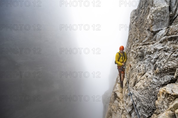 Mountaineers on a steep rock face on the Via Ferrata Oliva Detassis via ferrata in fog, steep