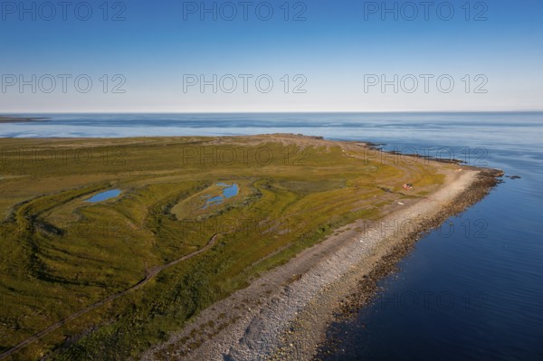 Coastal landscape on Varangerfjord with blue sky, still sea, moors and pebble beach aerial view,