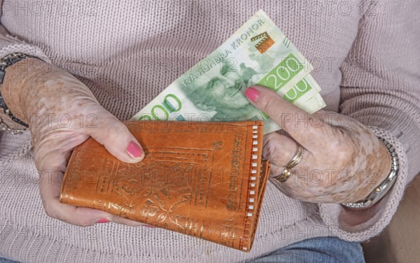 An elderly woman's hands take out Swedish banknotes from a wallet