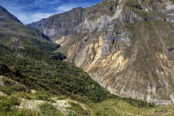 Wide valley surrounded by steep rock cliffs under blue skies, the landscape of the Colca Canyon in