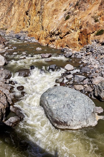 Close-up of a torrential river surrounded by boulders and orange cliffs, The landscape of the Colca