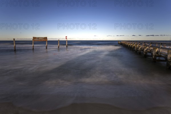 Wooden sign in the sea with inscription Zingst and wooden walkway, long exposure, evening light,